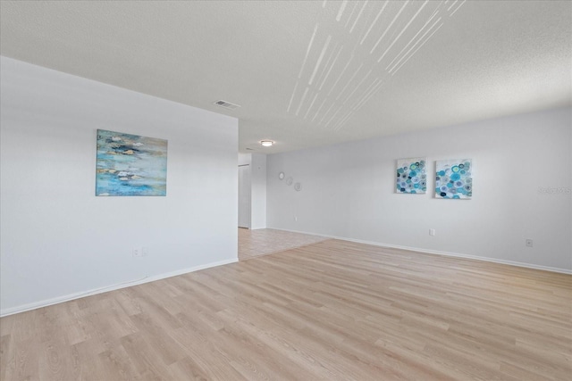 spare room with light wood-type flooring, baseboards, visible vents, and a textured ceiling