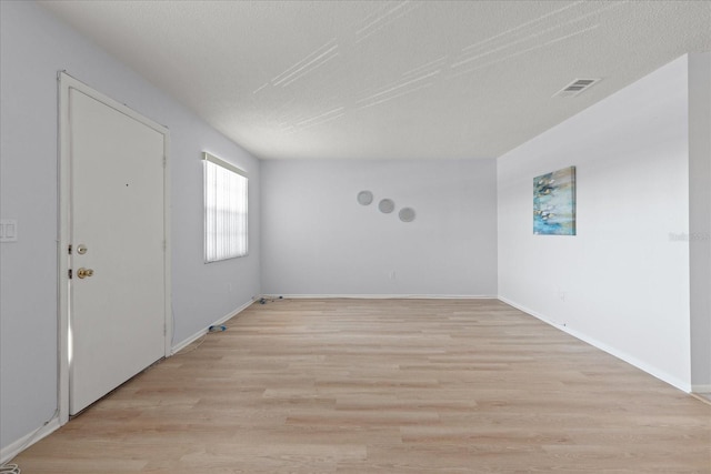 unfurnished room with a textured ceiling, light wood-type flooring, visible vents, and baseboards