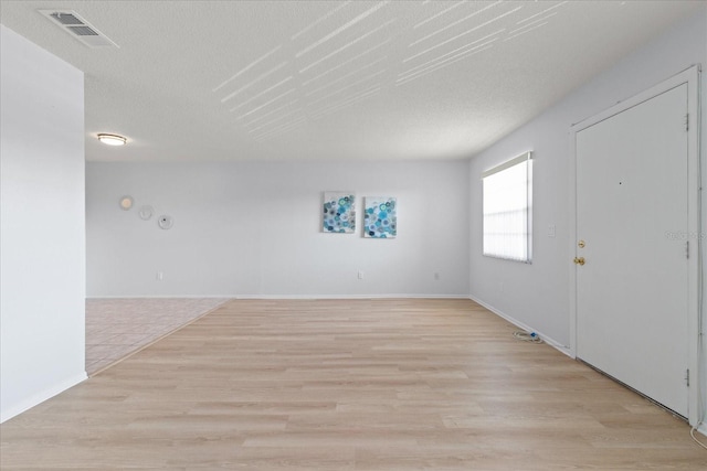 spare room with light wood-style floors, baseboards, visible vents, and a textured ceiling