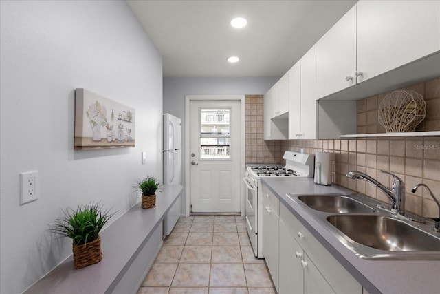 kitchen with white appliances, light tile patterned floors, white cabinets, decorative backsplash, and a sink