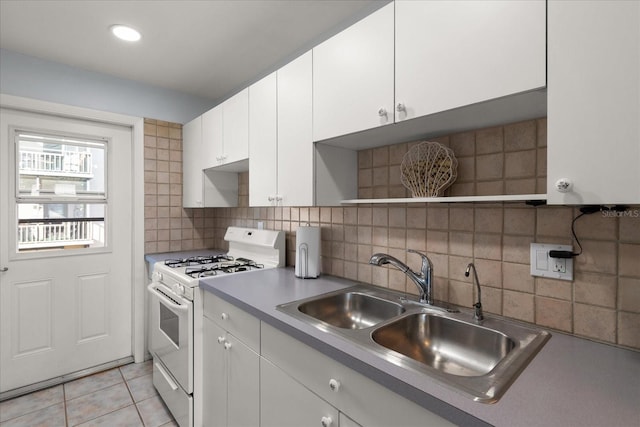 kitchen featuring light tile patterned floors, white gas stove, a sink, white cabinets, and decorative backsplash