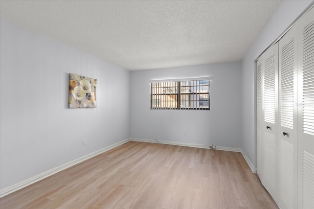 unfurnished bedroom with light wood-type flooring, a closet, a textured ceiling, and baseboards