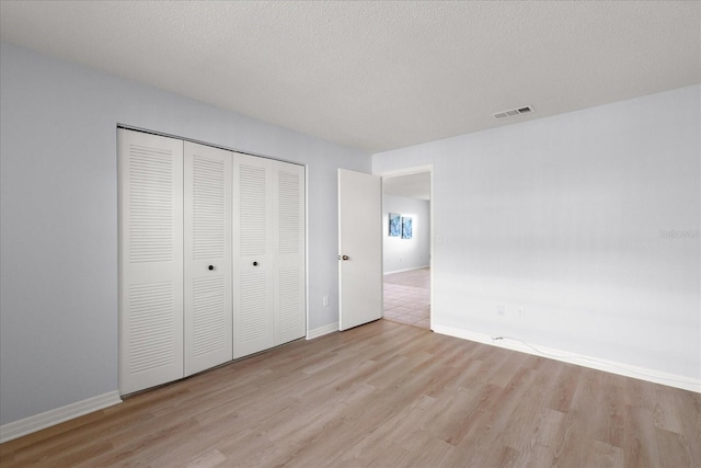 unfurnished bedroom featuring a closet, visible vents, a textured ceiling, and wood finished floors