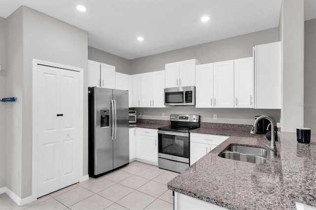 kitchen featuring light tile patterned floors, a sink, white cabinets, appliances with stainless steel finishes, and dark stone countertops