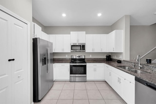 kitchen featuring light tile patterned floors, white cabinets, dark stone counters, appliances with stainless steel finishes, and a sink