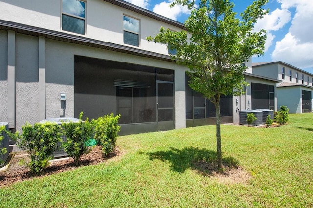 back of house featuring a lawn, cooling unit, a sunroom, and stucco siding