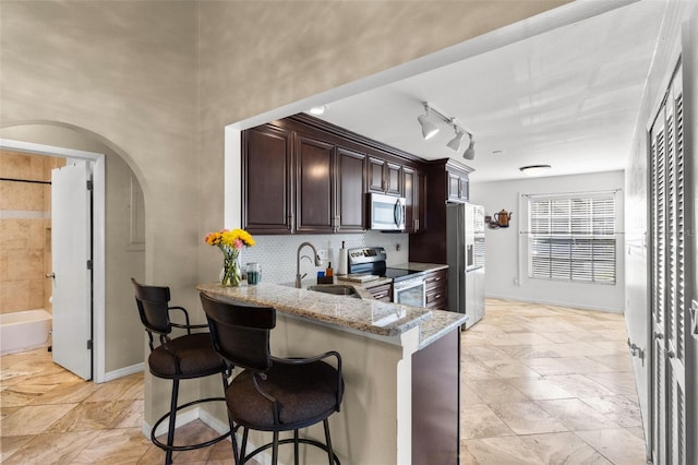 kitchen featuring tasteful backsplash, appliances with stainless steel finishes, light stone countertops, a kitchen bar, and a sink