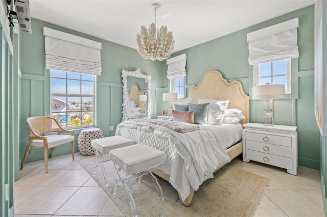 bedroom featuring wainscoting, a chandelier, a decorative wall, and light tile patterned flooring