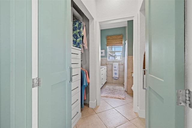 hallway featuring light tile patterned floors, wainscoting, and tile walls