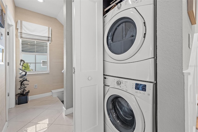 laundry area with stacked washer / dryer, laundry area, light tile patterned flooring, and baseboards