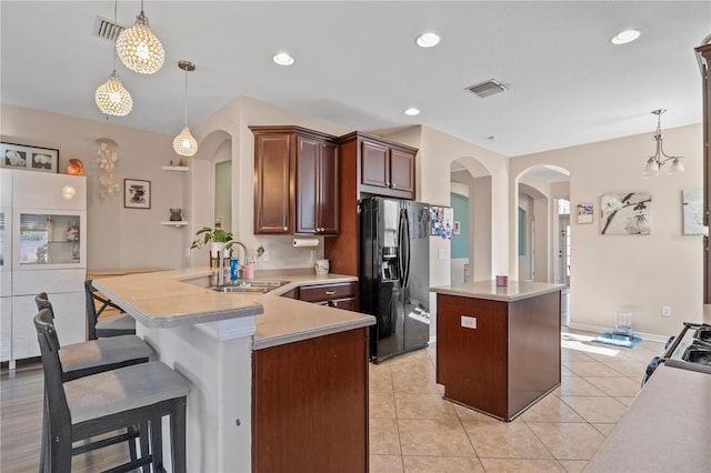 kitchen with arched walkways, black fridge with ice dispenser, a center island, light countertops, and a sink