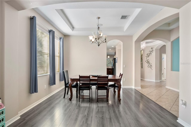 dining room with a tray ceiling, wood finished floors, visible vents, and an inviting chandelier