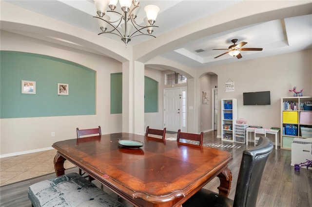 dining room with a tray ceiling, arched walkways, visible vents, wood finished floors, and baseboards