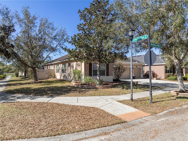 ranch-style home featuring a front yard, concrete driveway, an attached garage, and stucco siding