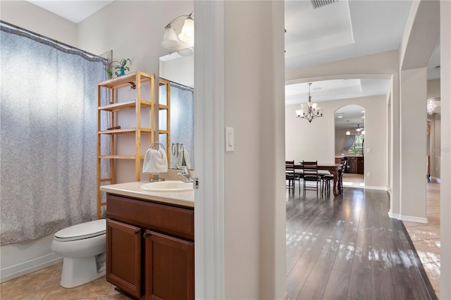 bathroom with toilet, a notable chandelier, wood finished floors, vanity, and shower / bath combo