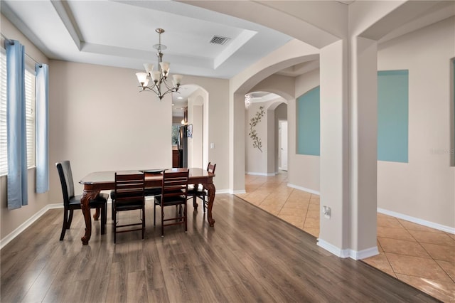 dining area featuring arched walkways, a raised ceiling, baseboards, and wood finished floors