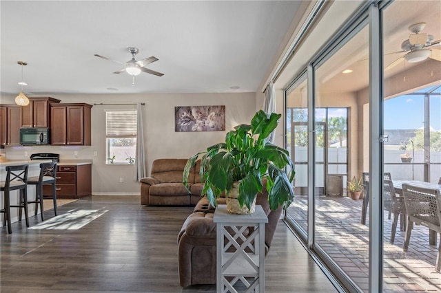 living room with baseboards, dark wood finished floors, and a ceiling fan