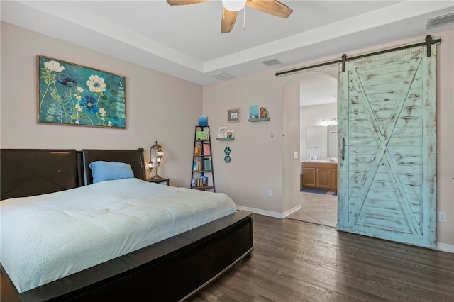 bedroom featuring a barn door, visible vents, arched walkways, and wood finished floors