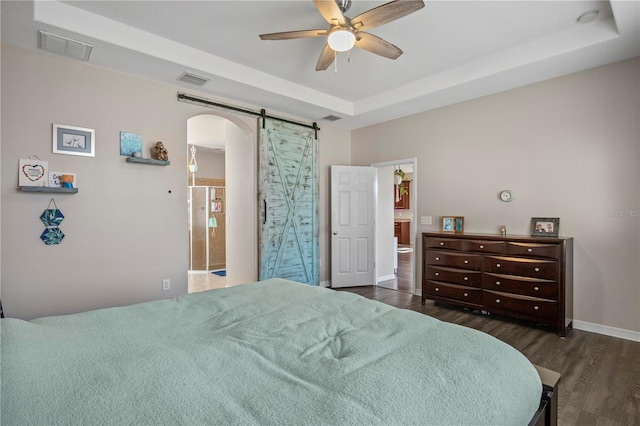 bedroom with arched walkways, a barn door, wood finished floors, visible vents, and a raised ceiling