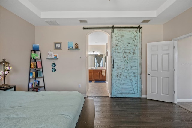 bedroom with a tray ceiling, visible vents, a barn door, and wood finished floors