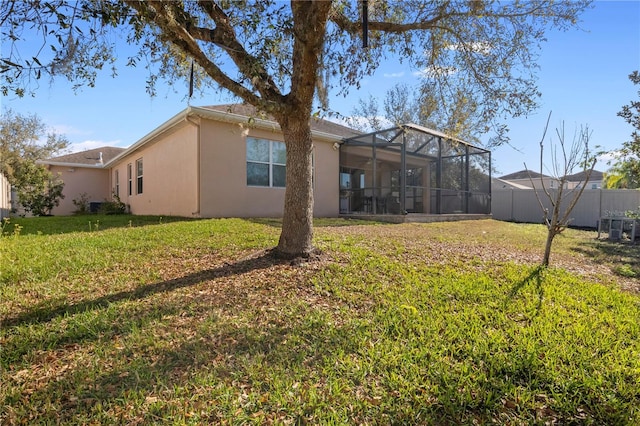 rear view of house with central AC unit, a fenced backyard, a lanai, a yard, and stucco siding