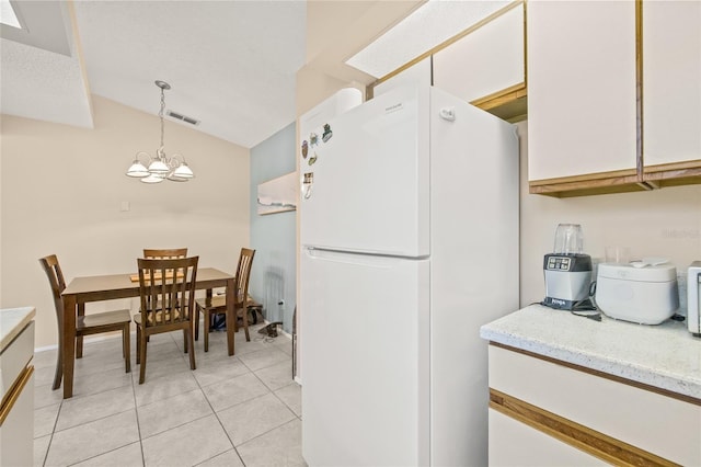 kitchen featuring light tile patterned floors, visible vents, white cabinets, freestanding refrigerator, and vaulted ceiling