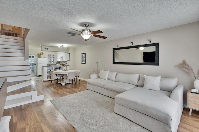 living room featuring visible vents, a ceiling fan, stairway, wood finished floors, and a textured ceiling