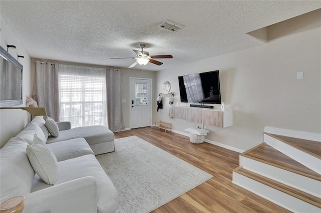 living area featuring a textured ceiling, wood finished floors, a ceiling fan, visible vents, and baseboards