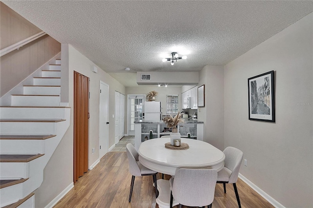 dining area featuring light wood-type flooring, a textured ceiling, baseboards, and stairs