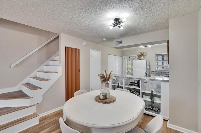 dining room with a textured ceiling, wood finished floors, visible vents, baseboards, and stairs