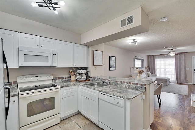 kitchen with visible vents, open floor plan, a sink, white appliances, and a peninsula