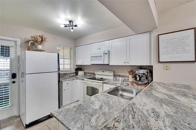 kitchen featuring white appliances, light tile patterned floors, light stone counters, white cabinetry, and a sink