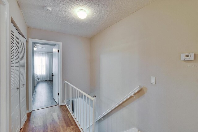 hall featuring a textured ceiling, wood finished floors, and an upstairs landing