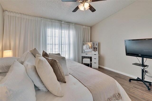 bedroom featuring lofted ceiling, a textured ceiling, baseboards, and wood finished floors