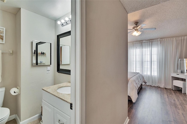 ensuite bathroom with toilet, ceiling fan, wood finished floors, a textured ceiling, and vanity