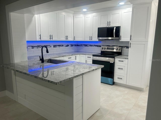 kitchen featuring light stone counters, a peninsula, a sink, white cabinets, and appliances with stainless steel finishes