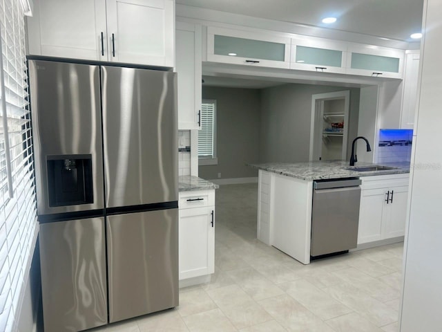 kitchen with light stone counters, white cabinets, stainless steel appliances, and a sink