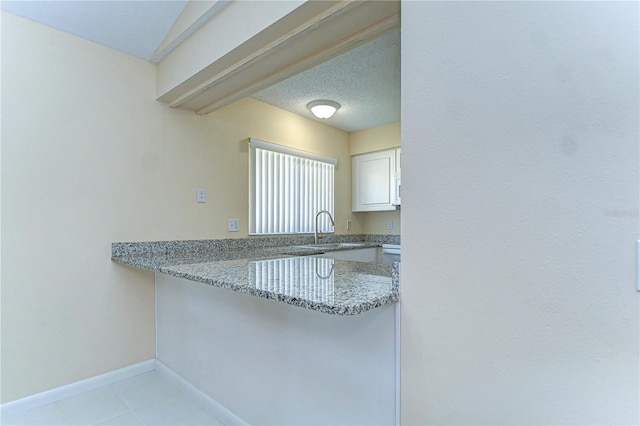 kitchen with white cabinetry, a sink, a textured ceiling, light stone countertops, and baseboards