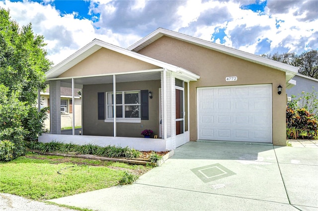 ranch-style home with concrete driveway, a sunroom, an attached garage, a front lawn, and stucco siding