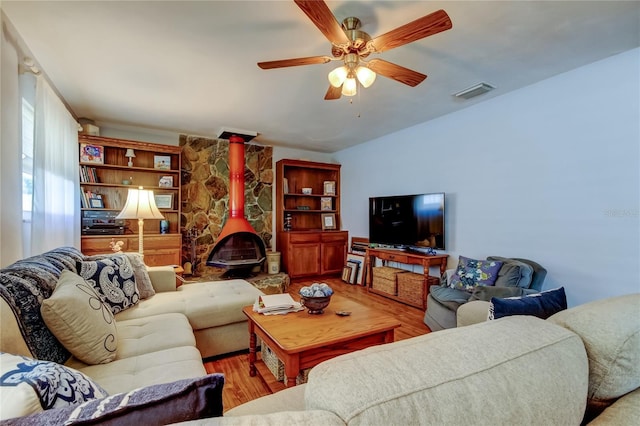 living area with a wood stove, a ceiling fan, visible vents, and wood finished floors