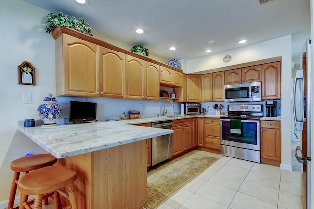 kitchen with light stone counters, a breakfast bar area, a peninsula, a sink, and appliances with stainless steel finishes