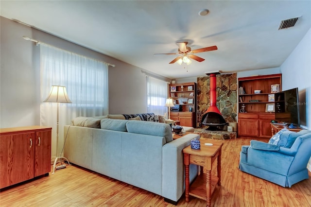 living area with a wood stove, light wood-style flooring, visible vents, and a ceiling fan