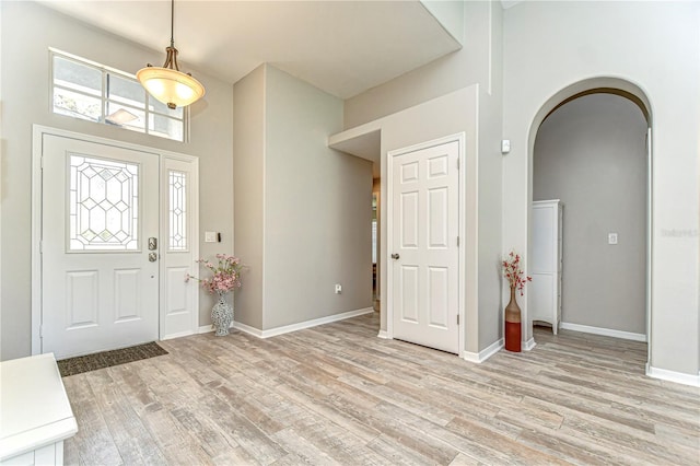 foyer featuring arched walkways, a high ceiling, light wood-type flooring, and baseboards