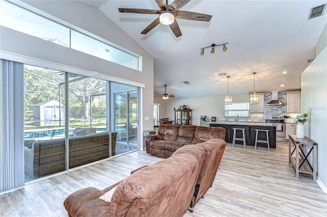 living room with high vaulted ceiling, visible vents, ceiling fan, and light wood finished floors