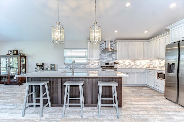 kitchen with stainless steel appliances, a sink, white cabinetry, decorative backsplash, and wall chimney exhaust hood