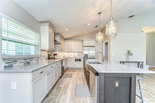 kitchen featuring light wood-style flooring, a sink, vaulted ceiling, appliances with stainless steel finishes, and tasteful backsplash