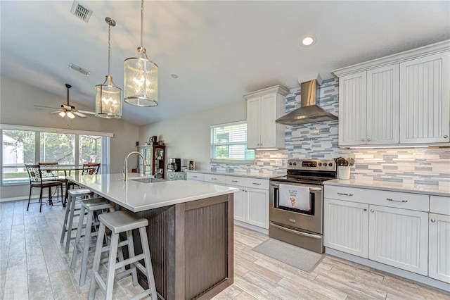 kitchen with electric stove, visible vents, a sink, and wall chimney range hood