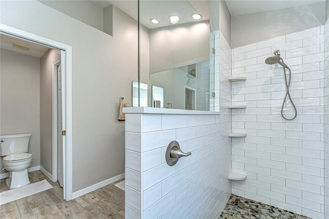 full bath featuring wood finished floors, a tile shower, toilet, and baseboards