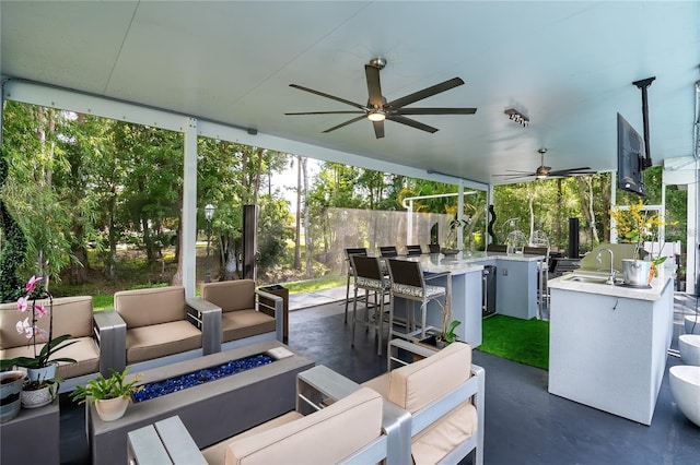 view of patio with a ceiling fan, an outdoor kitchen, a sink, and an outdoor living space with a fire pit