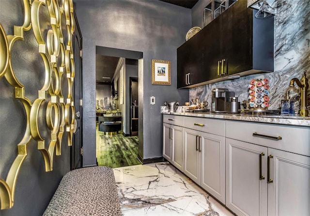 bar featuring tasteful backsplash, baseboards, marble finish floor, wet bar, and a sink